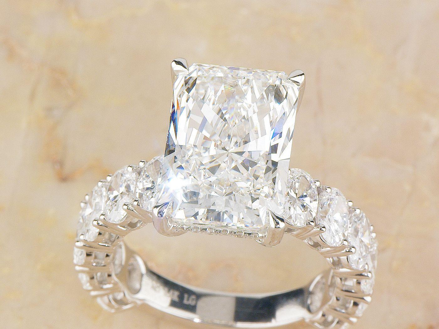 Radiant engagement ring with graduated oval side stones on marble